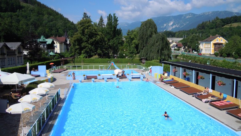 Payerbach outdoor pool with swimmers and surrounding landscape.