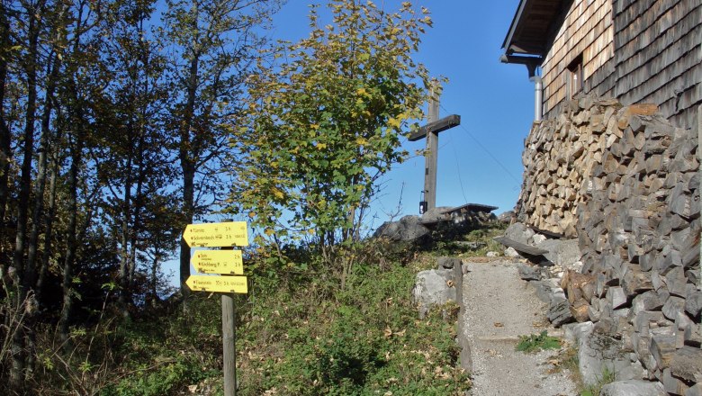 Signpost and wooden cross next to a wooden house in a mountainous landscape.