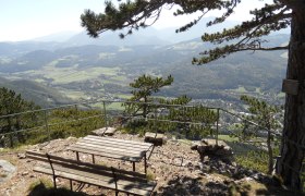 Viewpoint with bench and table, surrounded by trees, with a view of a valley and mountains in the background.