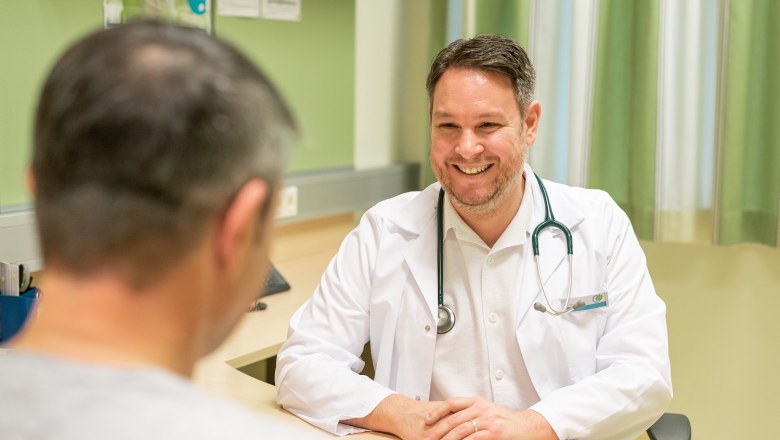 A doctor in a white coat smiles at a patient as they sit at a table.