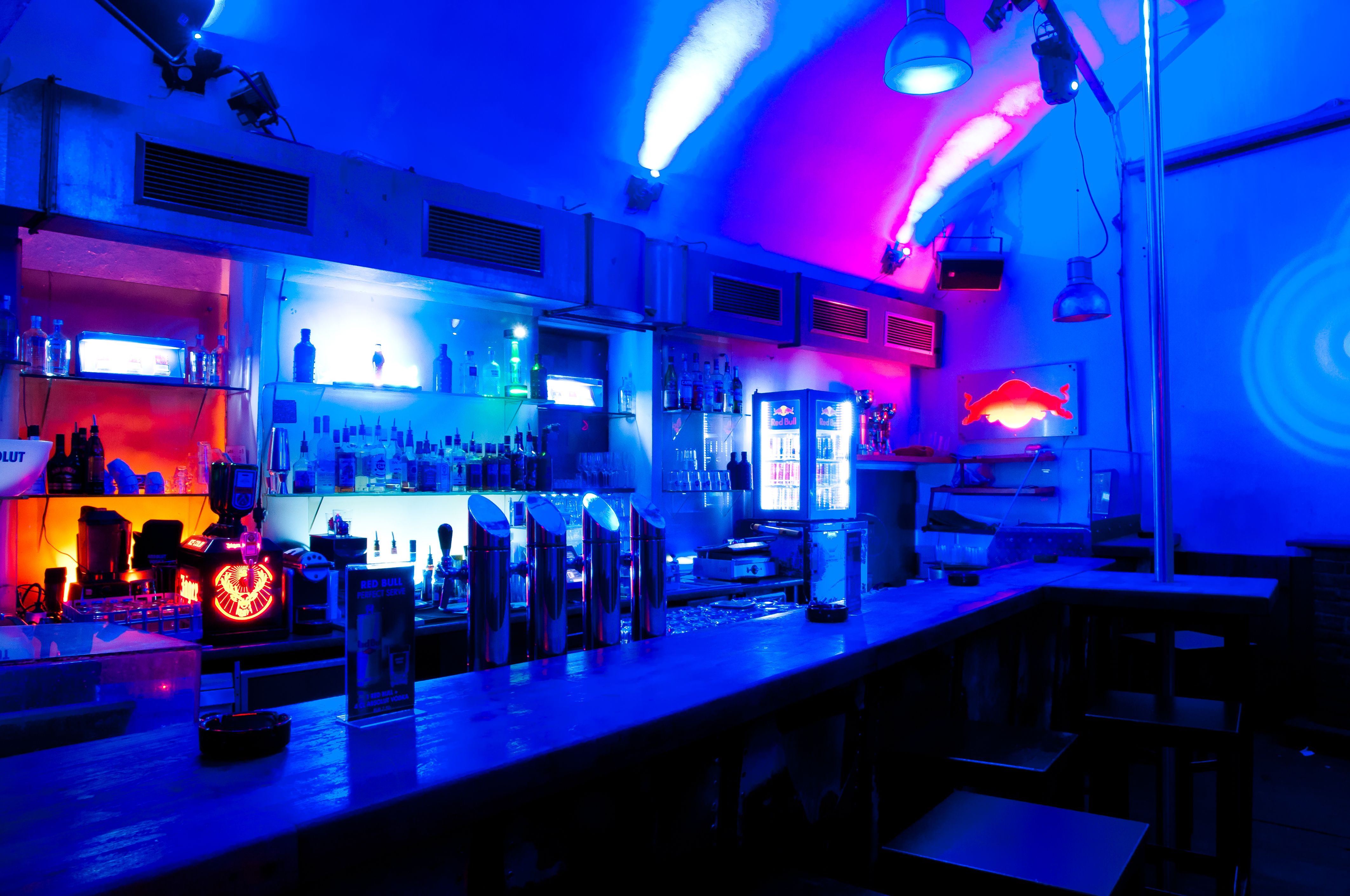 Bar with blue and red lighting, bottles and glasses on the shelf.