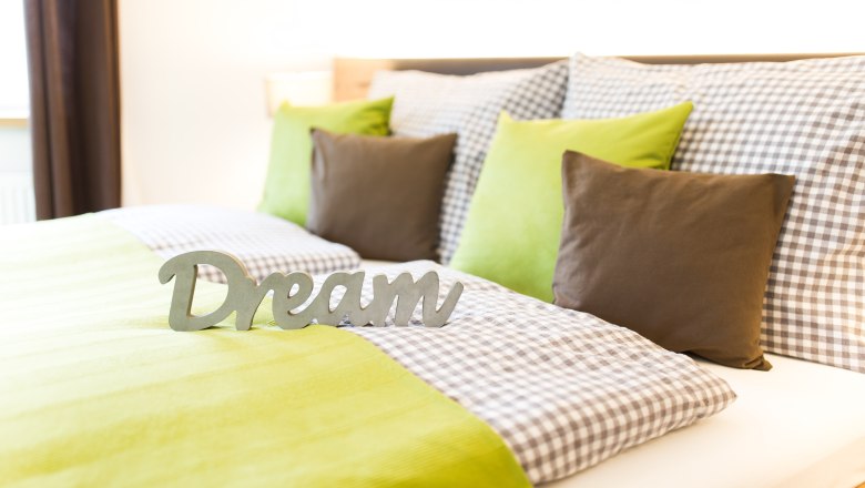 Cozy bed with green and checkered bed linen, decorated with pillows and a 'Dream' lettering.