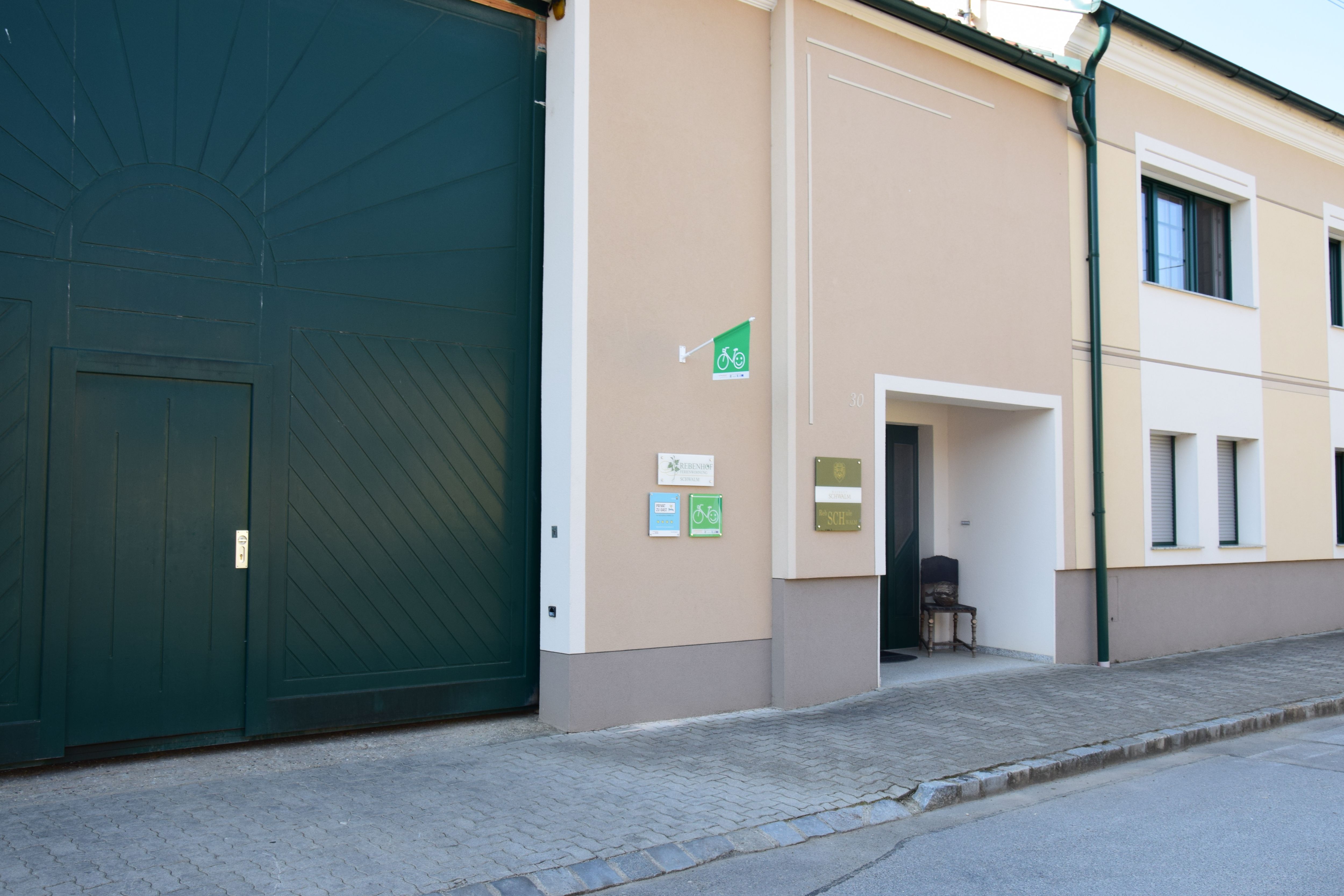 Entrance to a winery with large green gates and signs on the wall.