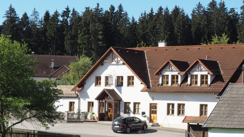 A traditional inn with a white façade and brown roof, surrounded by trees and meadows.