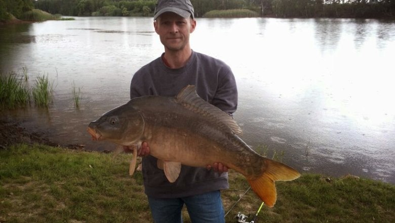A man holds a large fish in front of a lake.