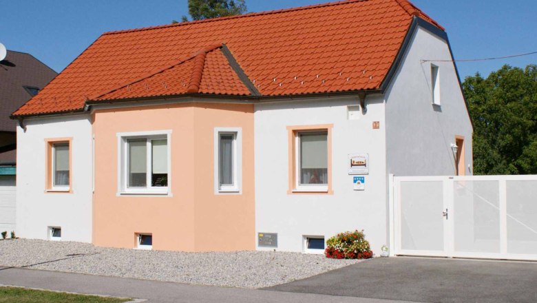A small, single-storey house with an orange roof and white façade under a blue sky.