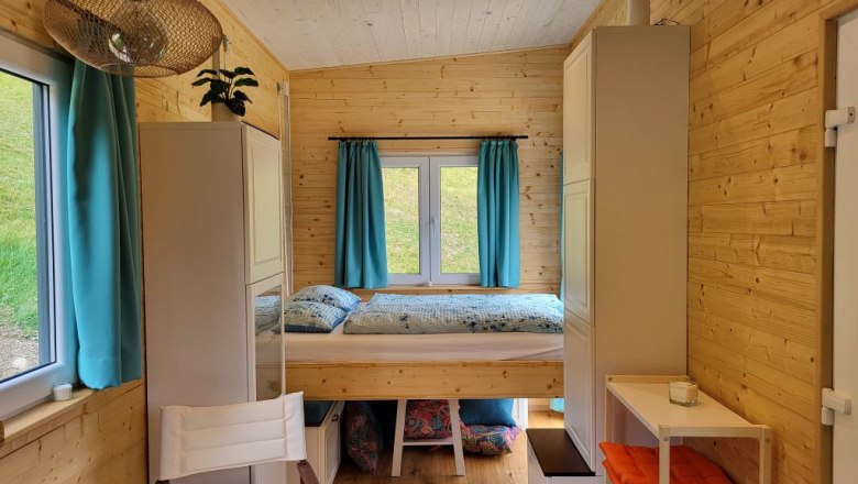 Small room with wooden walls, fold-down bed, blue curtains and shelves.