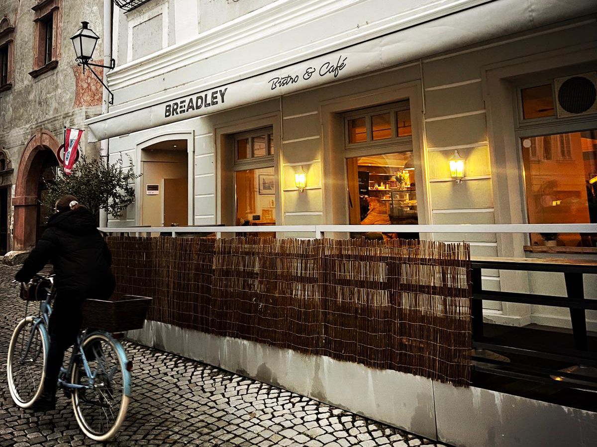 Exterior view of a café with a cyclist on cobblestones.