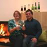A couple is sitting in front of a fireplace, clinking glasses of wine.