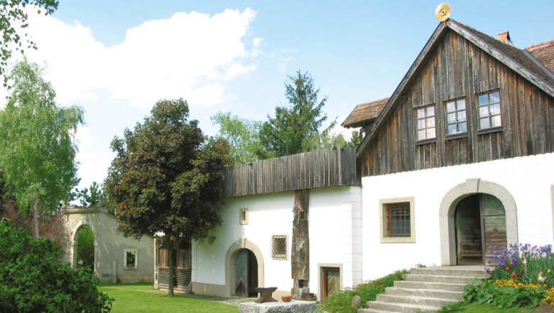 A traditional building with a wooden roof and white fa&ccedil;ade, surrounded by a green garden.