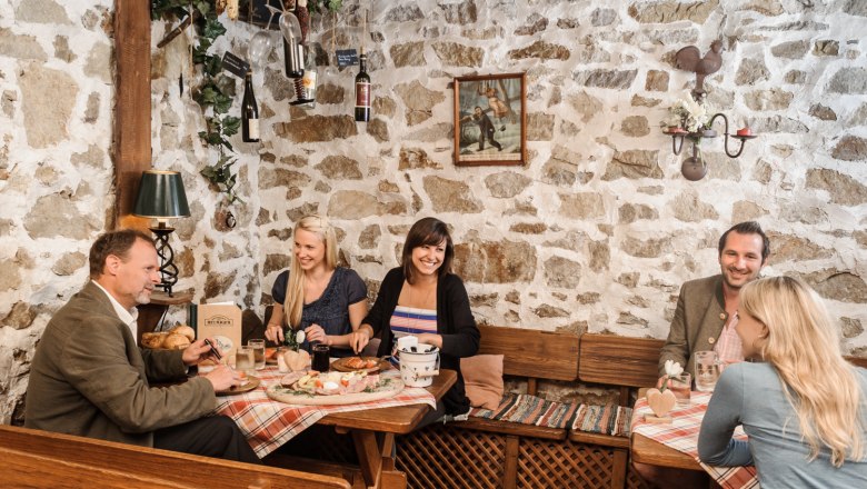 Group of people in a traditional wine tavern with stone walls, food and wine.