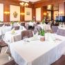 Elegant restaurant with laid tables, white tablecloths and plants.