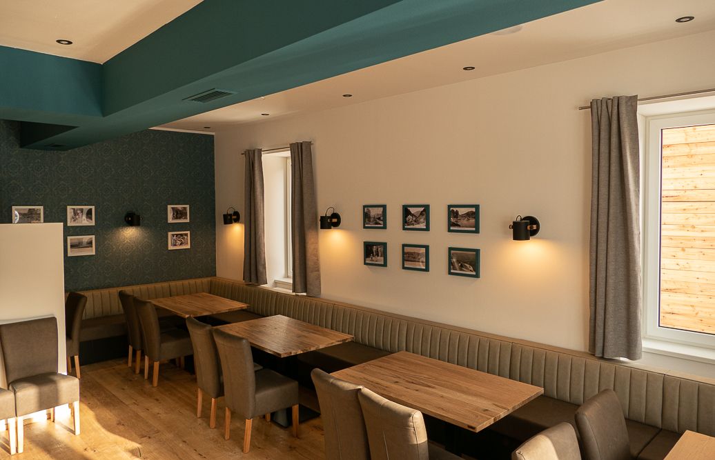 Interior view of a restaurant with wooden tables, upholstered benches and chairs, decorated with pictures on the walls.