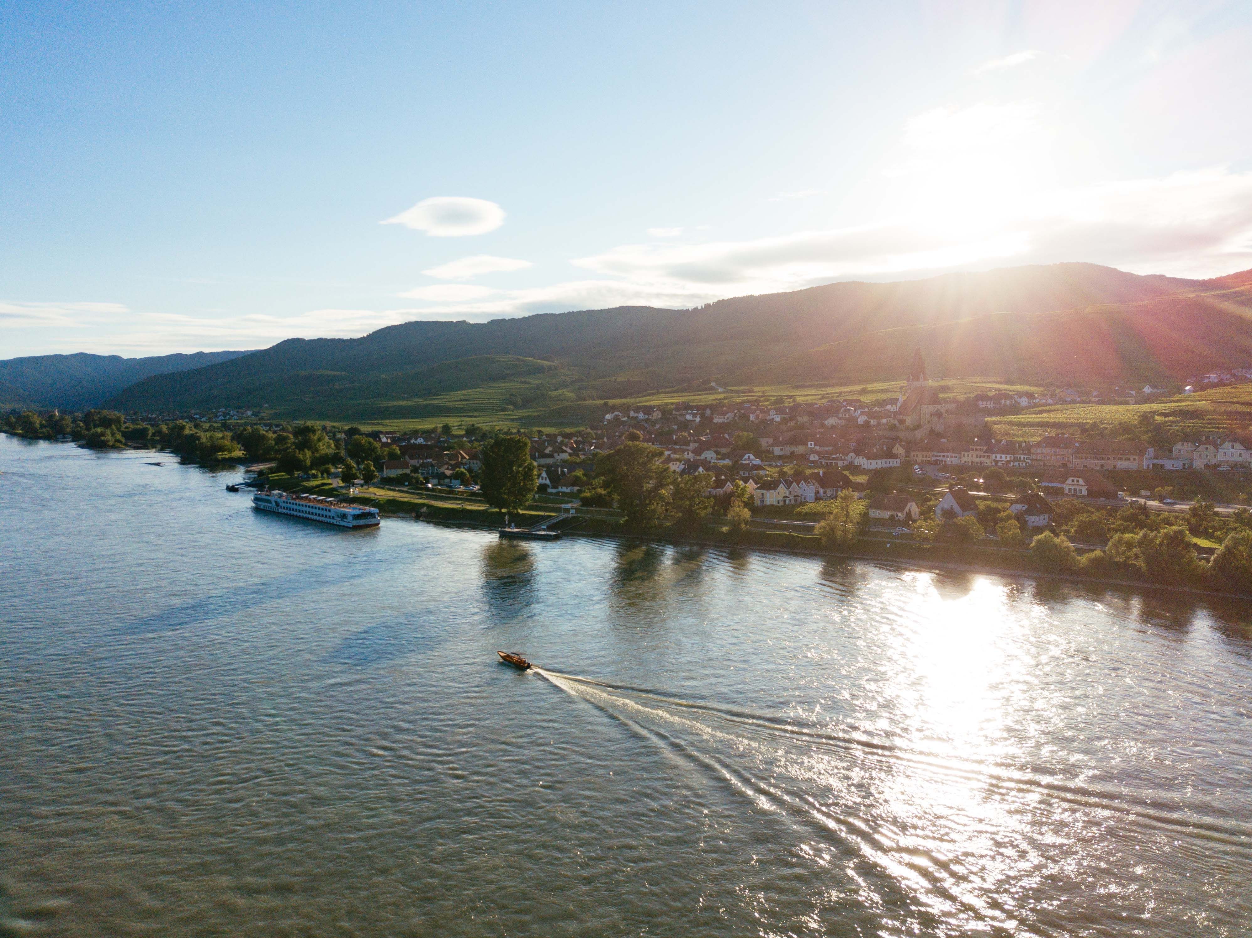 Aerial view of the Wachau with river, boats and village at sunset.
