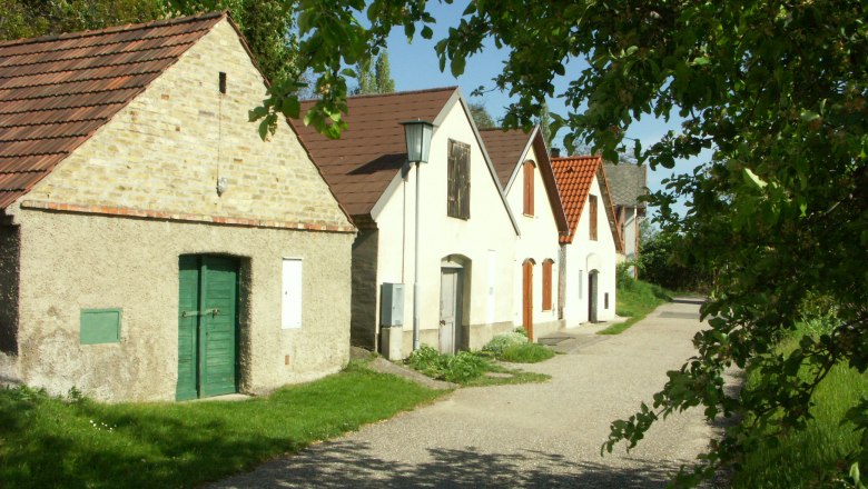 A picturesque wine cellar lane with old wine cellars and green trees.