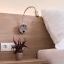 Close-up of a bed with wooden back panel, reading lamp, sockets and potted plant.