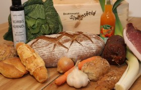 Various foods such as bread, vegetables, oil and sausage on a table.