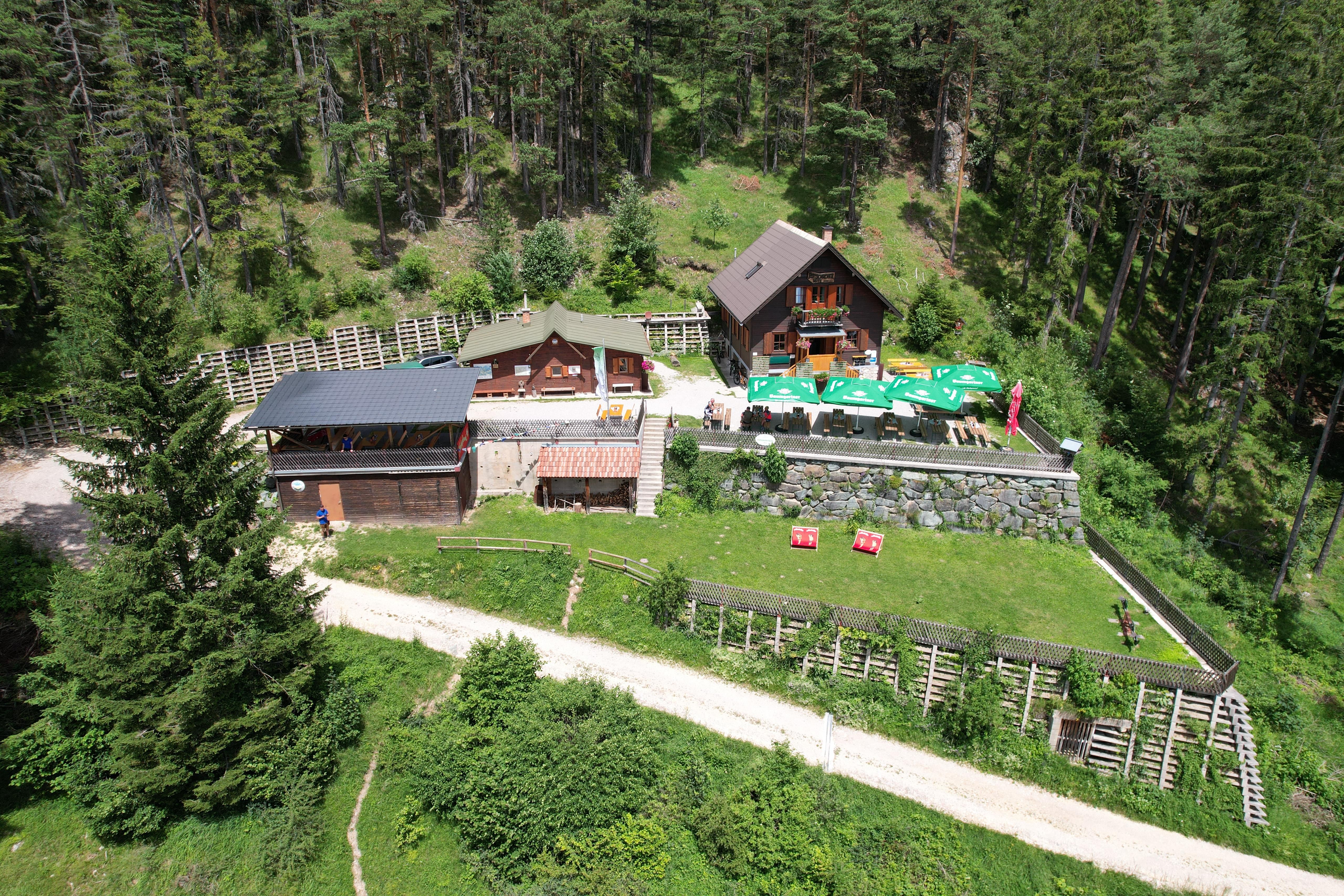 Aerial view of the Potschacherhütte in a wooded area with surrounding trees and a terrace with sunshades.