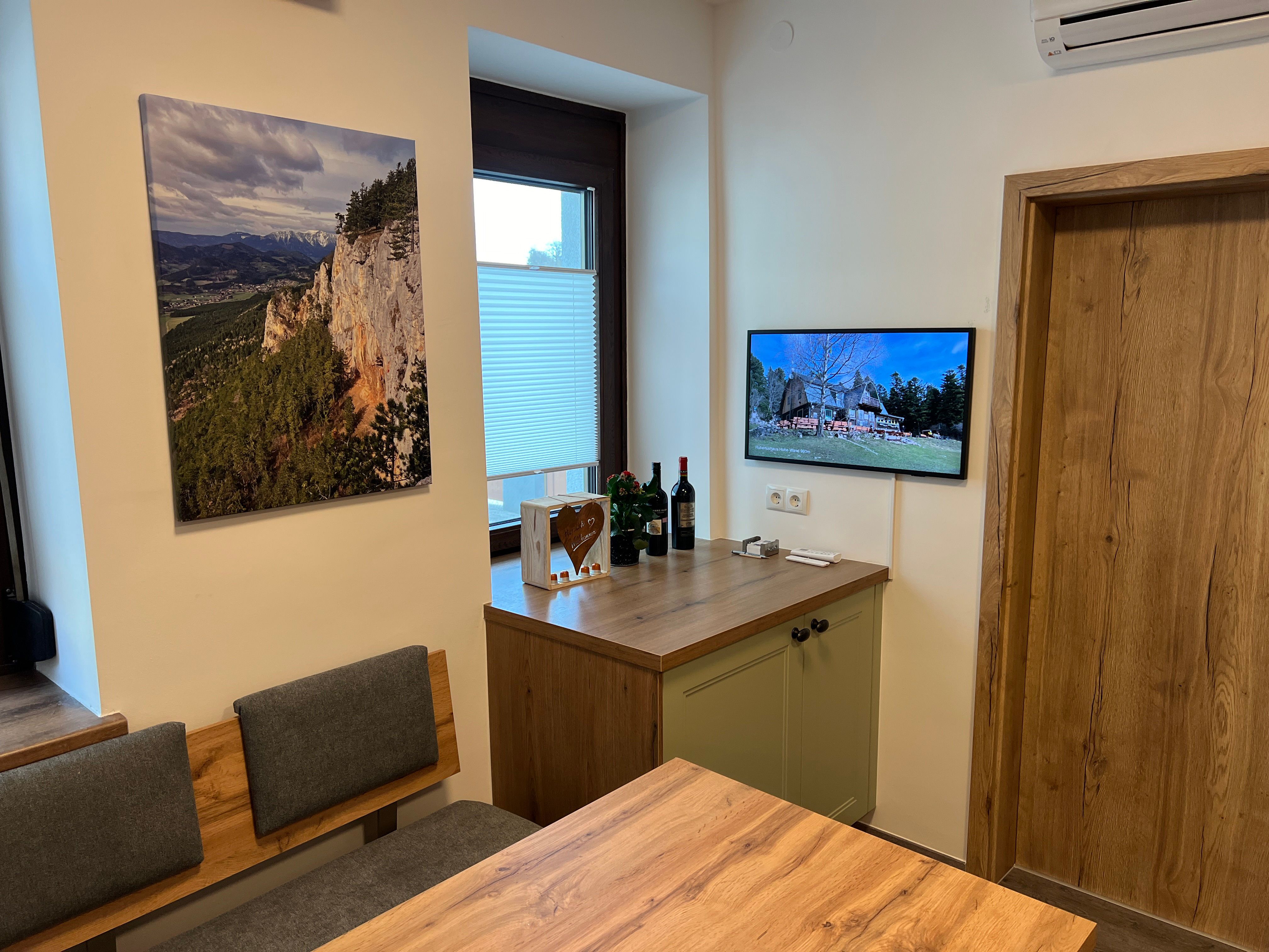 Kitchen with wooden furniture, a landscape painting on the wall and a TV showing a picture of a house.