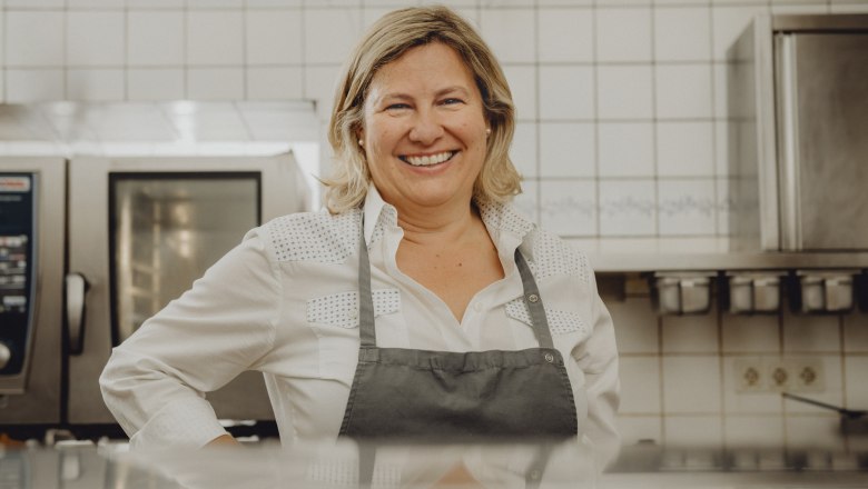 A smiling woman in a kitchen wearing an apron.
