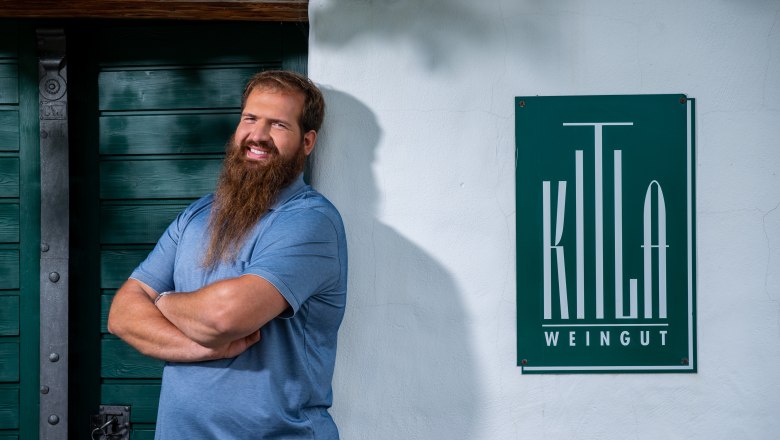 A man with a beard stands smiling in front of a sign that reads 'Kitla Winery'.