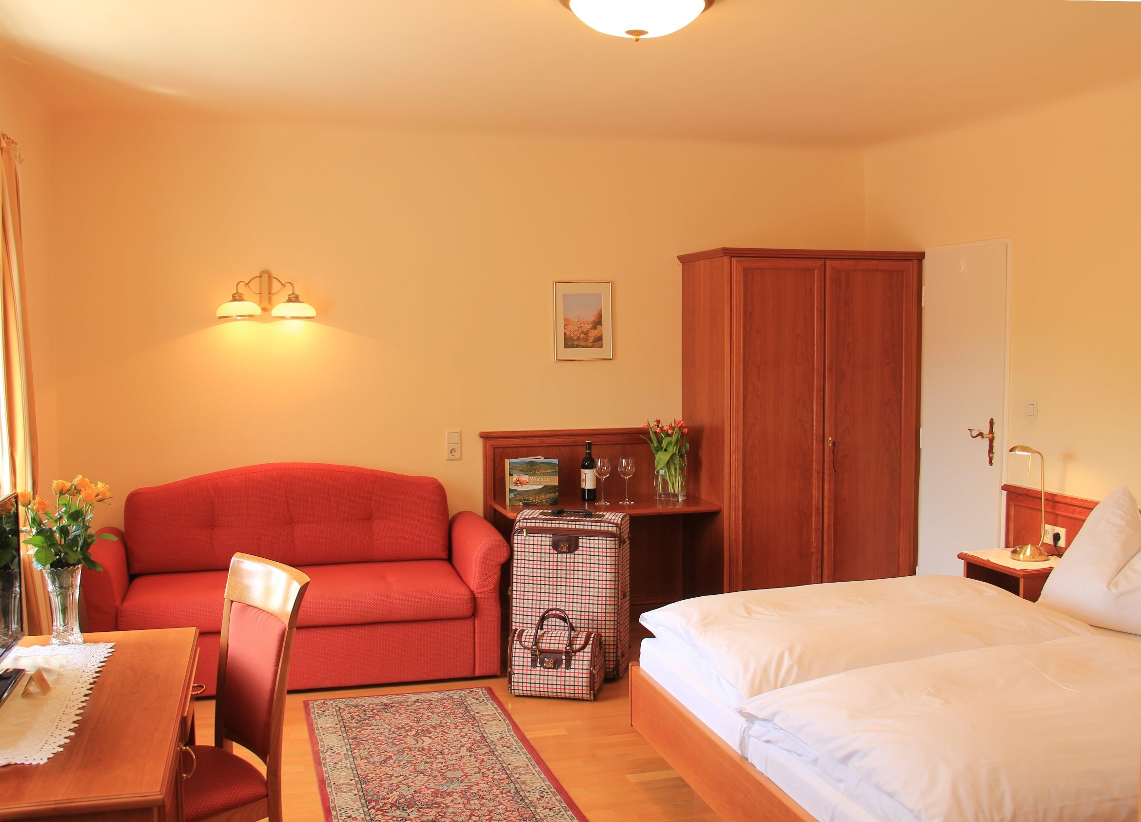 A cozy hotel room with a double bed, red sofa, wooden furniture and flowers.