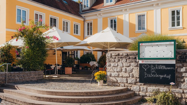 Yellow historic building with terrace and parasols, surrounded by plants.