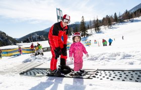 A ski instructor helps a small child to ski on a conveyor belt in the snow.