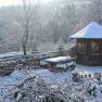 Snowy landscape with wooden hut, wooden fence and forest in the background.