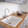 Modern kitchen unit with sink, wooden worktop and basket with utensils.