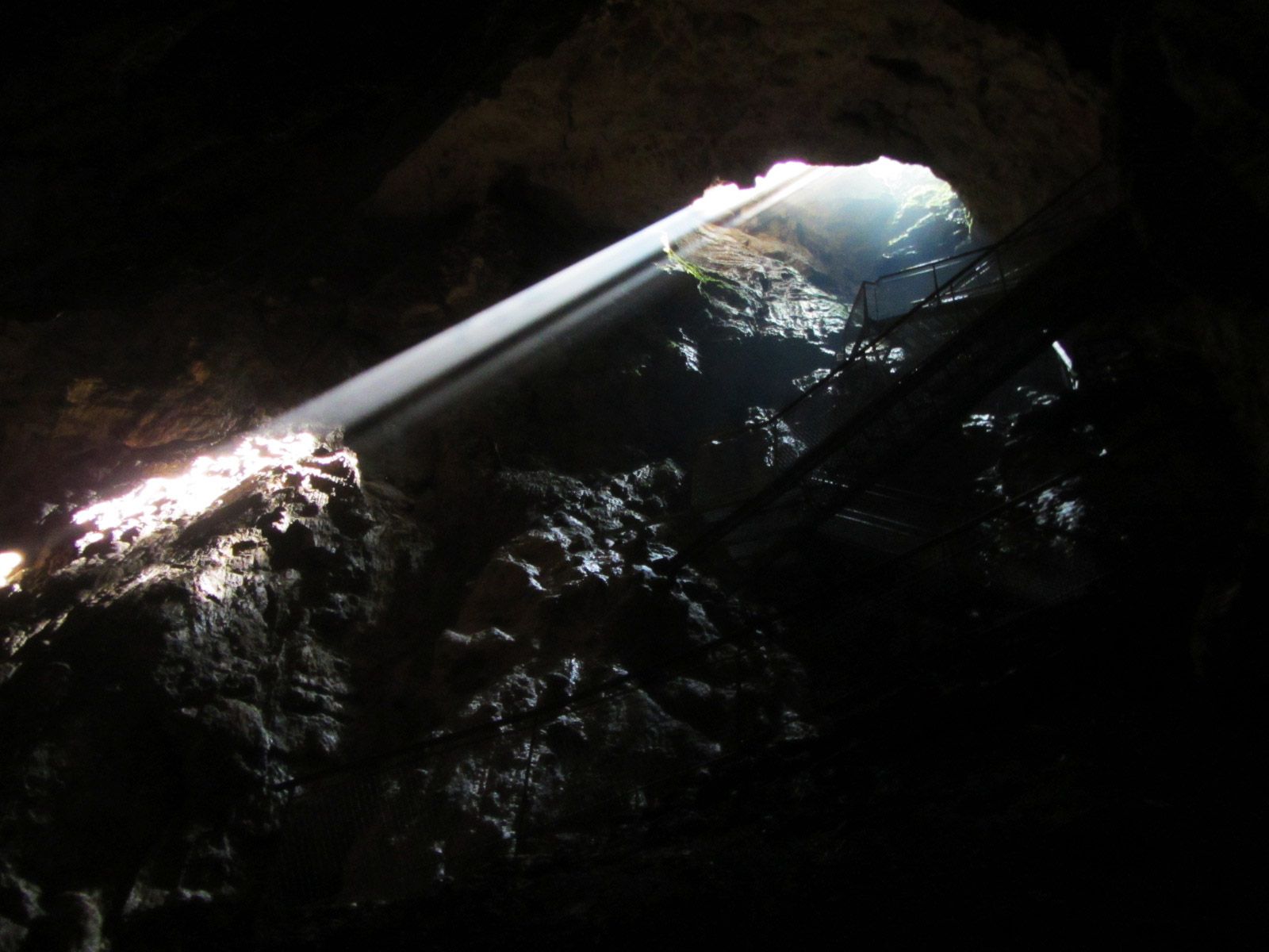 Rays of sunlight penetrate through an opening in a dark stalactite cave.