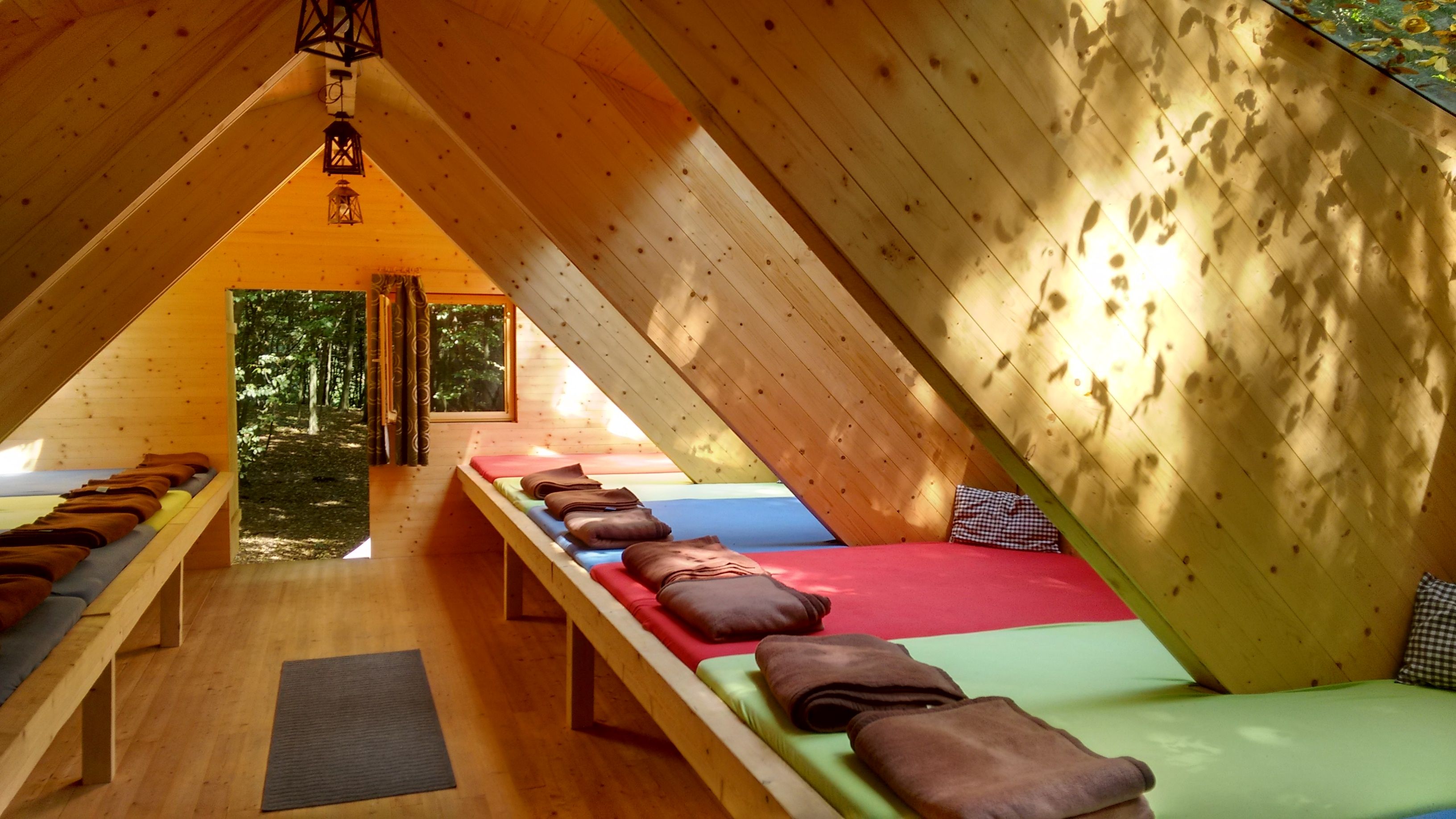 Interior view of a wooden hut dormitory with mattresses and blankets.