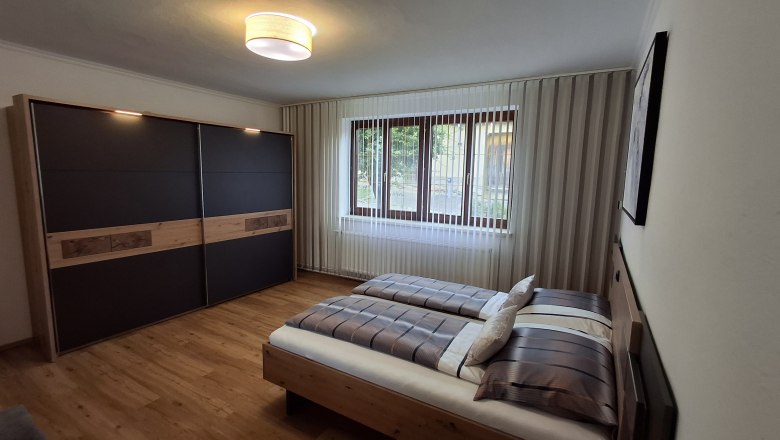 Modern bedroom with double bed, large closet and window with blinds.