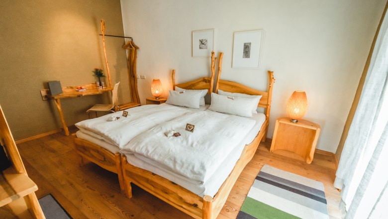 Wooden room, © Matthias Auer A cozy bedroom with wooden furniture, a double bed, bedside tables and a desk. Two lamps and pictures on the wall complete the ambience.