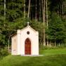 A small chapel with a cross on the roof, surrounded by trees and grass.