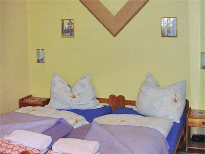 Two single beds in a room with a yellow wall and decorative pictures.