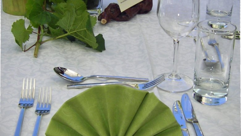 Elegant table decoration with green folded napkin, cutlery, wine glass and water glass on a white tablecloth.