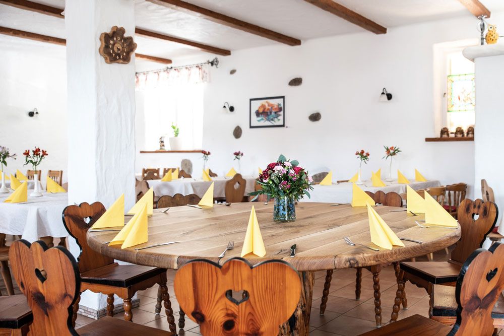 A cozy room with wooden tables and chairs, yellow napkins and flower arrangements.