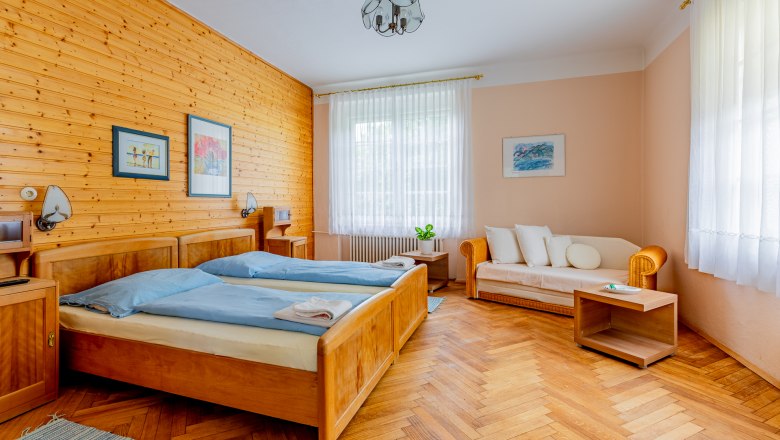 Cozy bedroom with wooden walls, two beds, sofa and wooden floor.