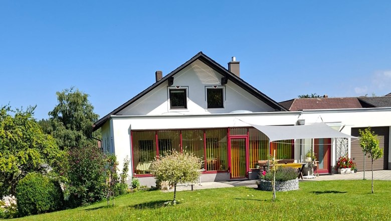 House view, © Ferienwohnung Penz Stolzenthal, Fotograf Hermine Penz A white house with a red frame and garden against a blue sky.