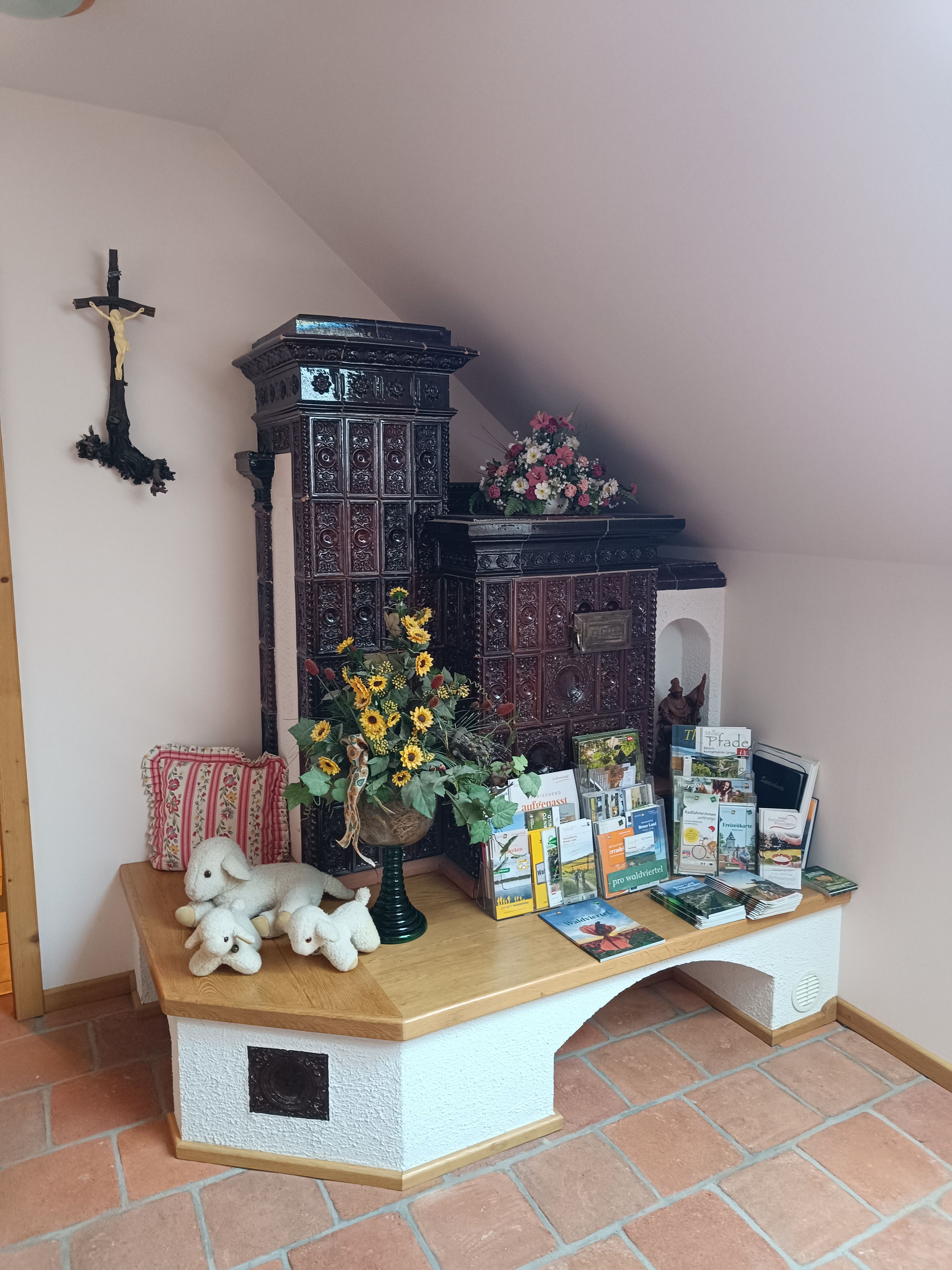 A traditional tiled stove in a room decorated with brochures, stuffed animals and flowers.