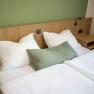 A double bed with white bed linen and a green wall in the background.