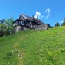 A mountain hut on a green meadow under a blue sky.