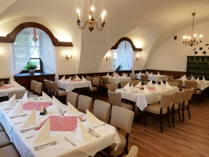 Guest room with laid tables, white tablecloths and red napkins, chandeliers and vaulted ceiling.