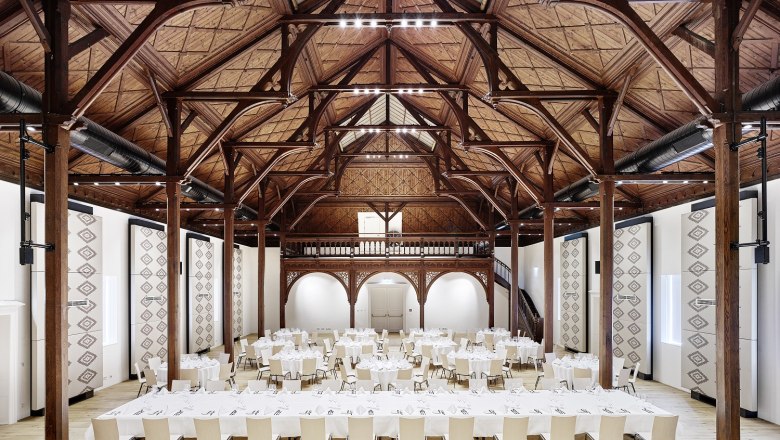 Interior view of a large banqueting hall with wooden beamed ceiling and covered tables.