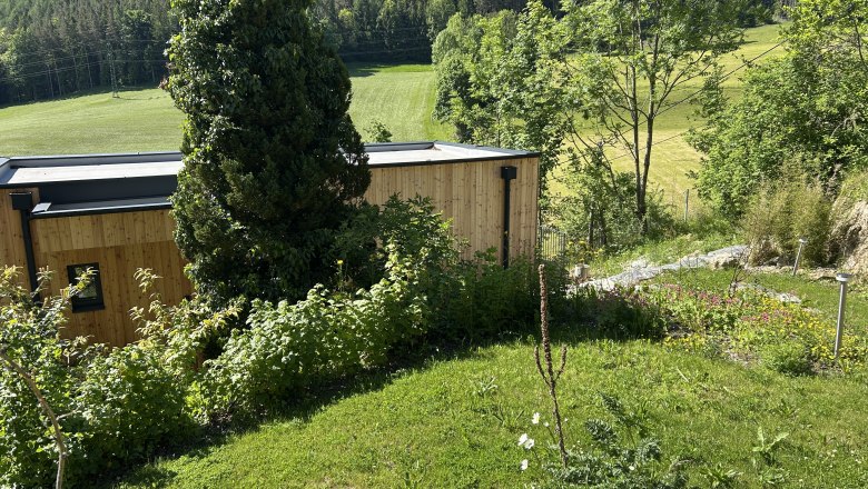 A modern wooden house in a green, hilly landscape with trees and meadows.