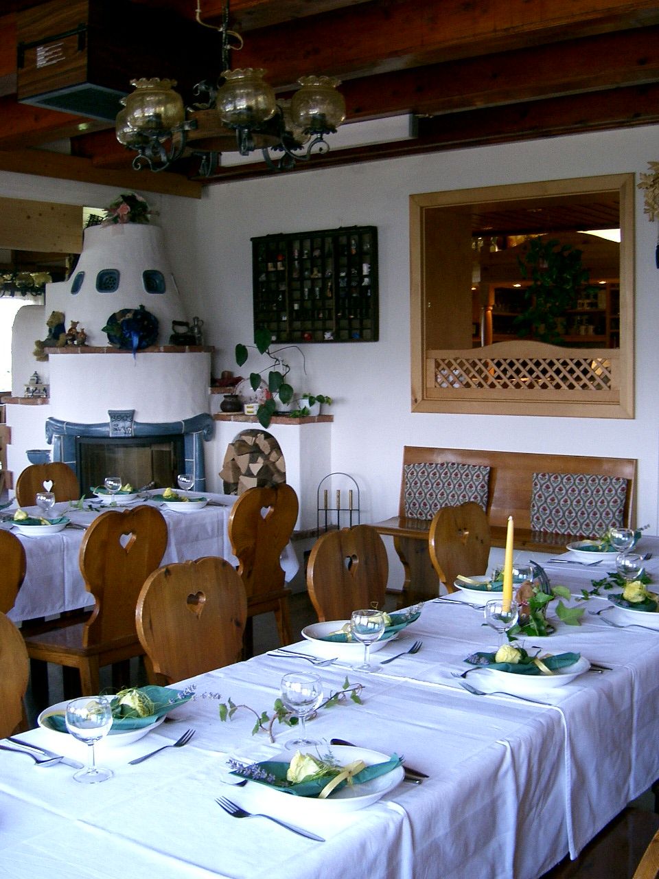 Cozy dining room with set tables, wooden furniture and tiled stove.