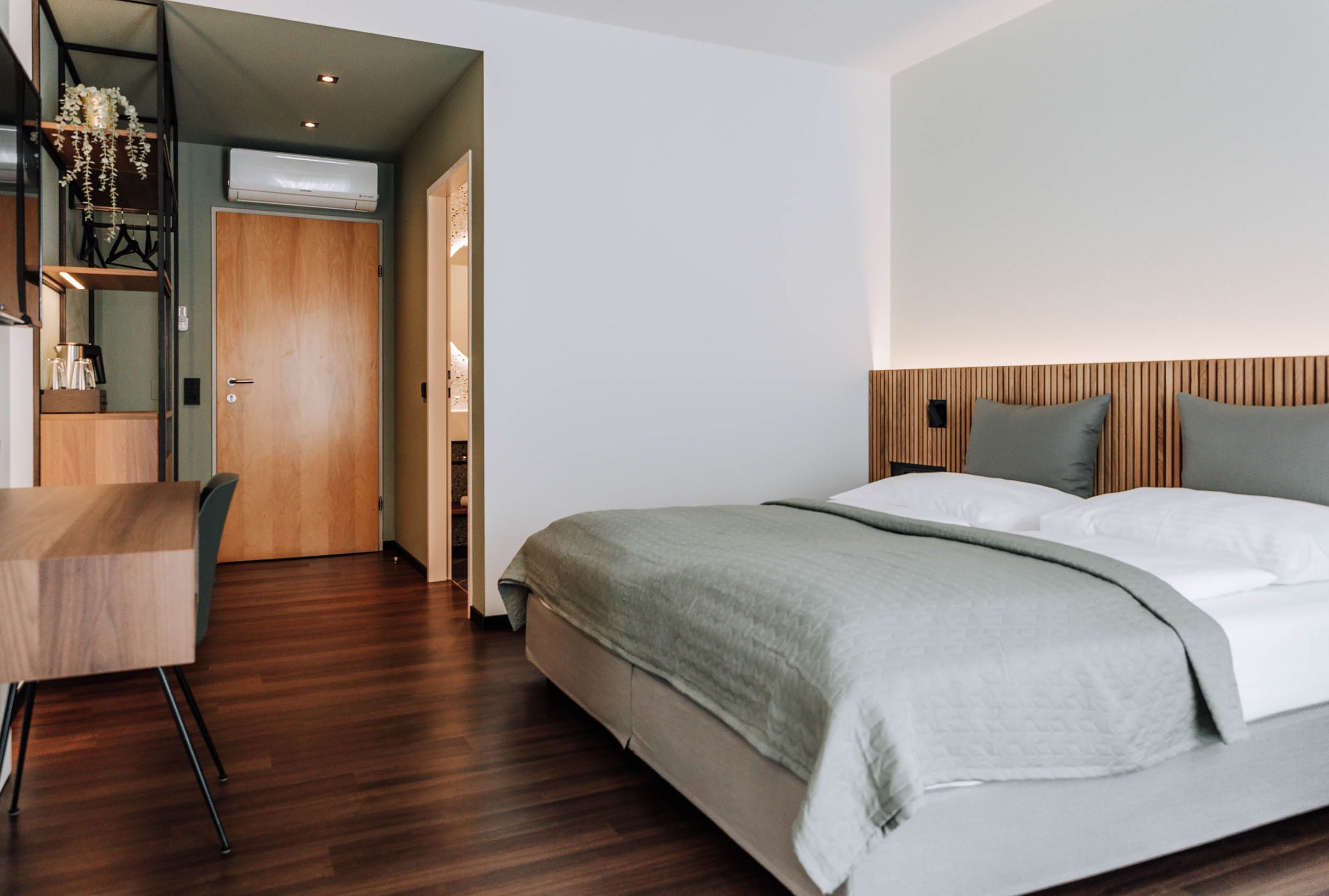 Modern hotel room with double bed, wooden floor and desk.