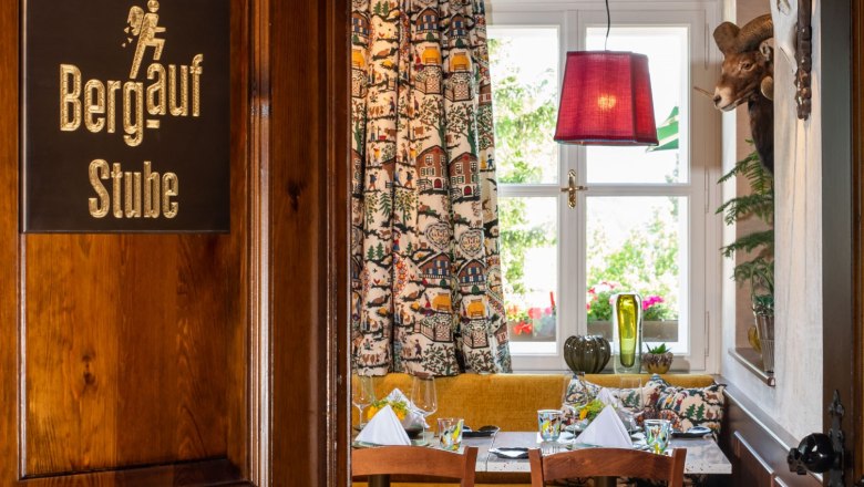 A cozy room in a restaurant with wooden furniture, a table with laid crockery, colorful curtains and antlers on the wall.