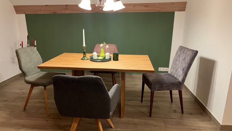 A dining table with four chairs in a room with a green accent wall and wooden floor.